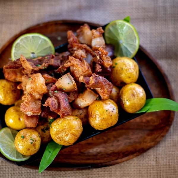 Crispy fried pork belly pieces and roasted baby potatoes garnished with lime wedges and herbs.